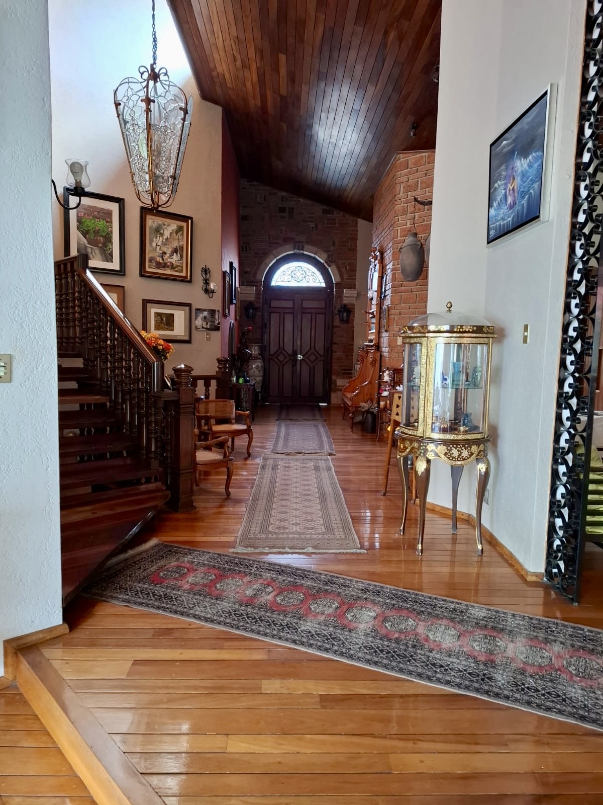 Vestíbulo con escalera de madera, candil emplomado y techos a dos aguas